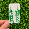 A hand with a French tip manicure holds a white display card featuring a pair of dangling earrings. The earrings are bright green with white script lettering that reads Chipmunks and are suspended from silver hooks.