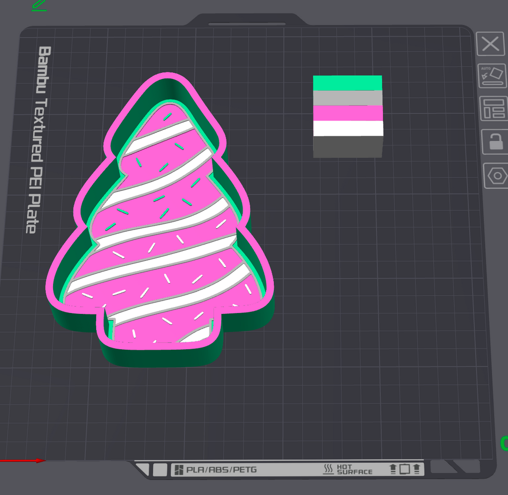 A 3D digital preview of a textured PET plate shaped like a Christmas tree, featuring pink frosting-like stripes, white sprinkles, a green inner layer, and a dark gray outer frame. It is displayed on a dark gray grid design screen with a color swatch in the top right.