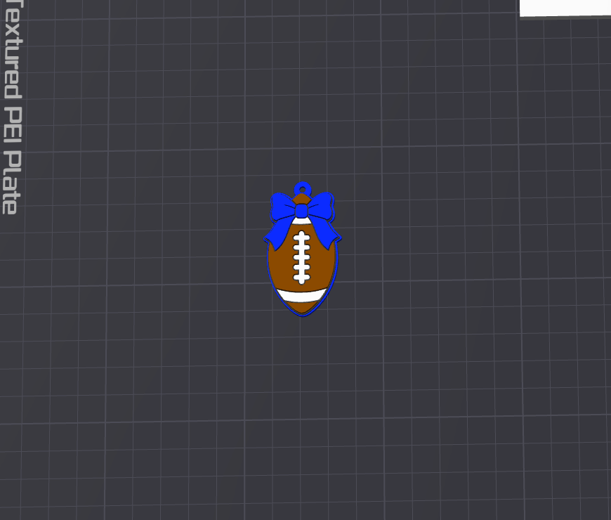 A small football-shaped charm or pendant with a blue ribbon bow at the top, shown centered on a dark gray grid background. The football is brown with white laces and a white band near the bottom.