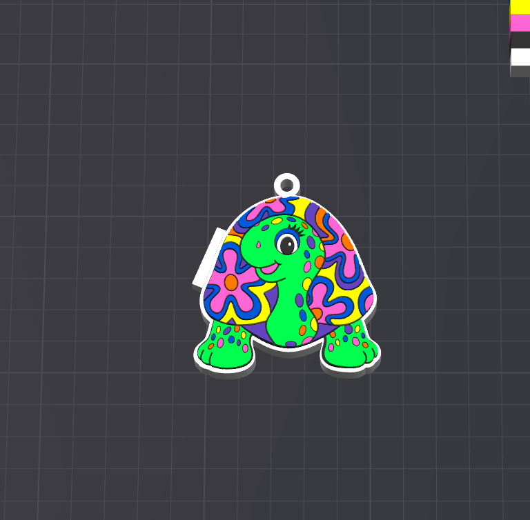 A colorful turtle-shaped charm or pendant with a white border and a small hanging loop at the top, shown on a dark gray grid background. The turtle has a bright green body and a patterned shell with pink, blue, yellow, and purple shapes.