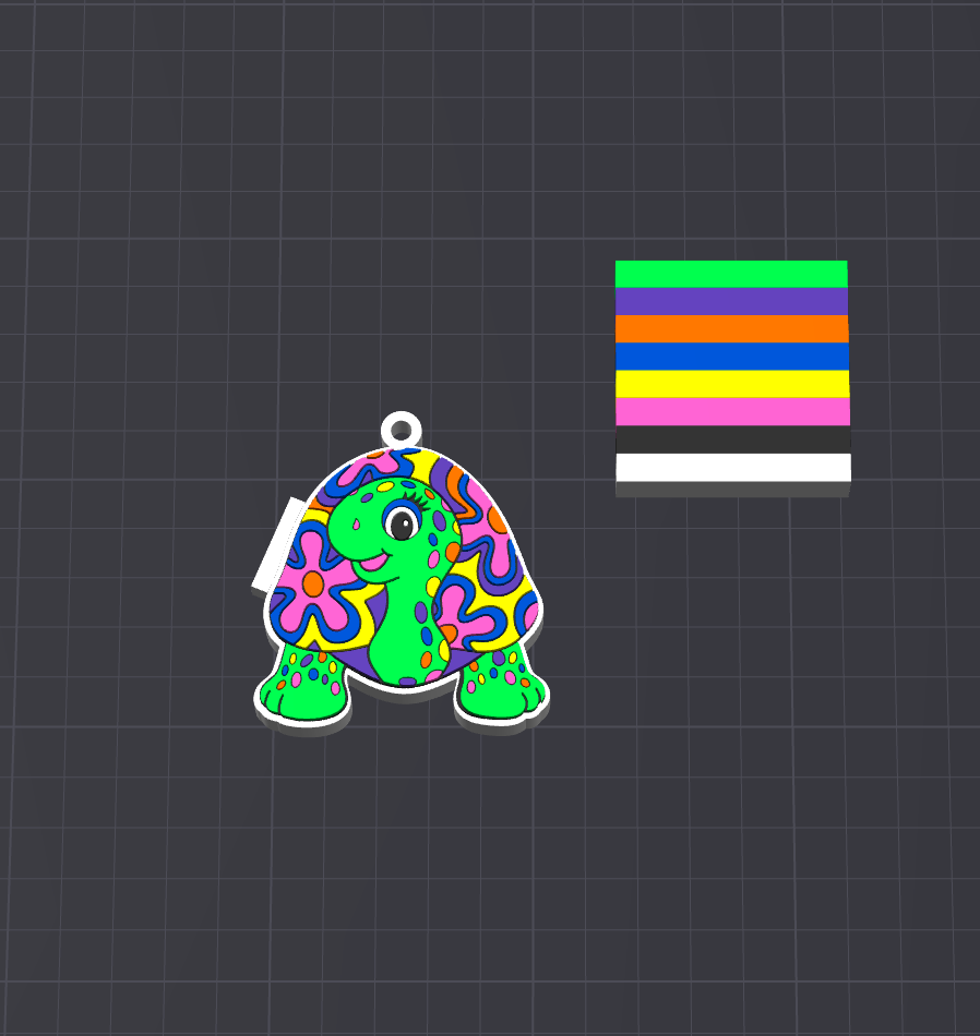 A colorful cartoon turtle charm with a white loop at the top, decorated with a vibrant psychedelic floral pattern in green, pink, purple, blue, and yellow. It is displayed on a dark gray grid background next to a color swatch strip showing the primary colors.