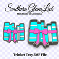 Digital product listing graphic for a Southern Glam Lab 'Trinket Tray 3MF File' featuring two 3D renders of a gray metal tray shaped like a stack of turquoise and white books tied with a bright pink ribbon, on a checkered transparency-style background.